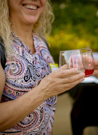 Two women holding drinks and clinking glasses, one wearing a name tag that says 