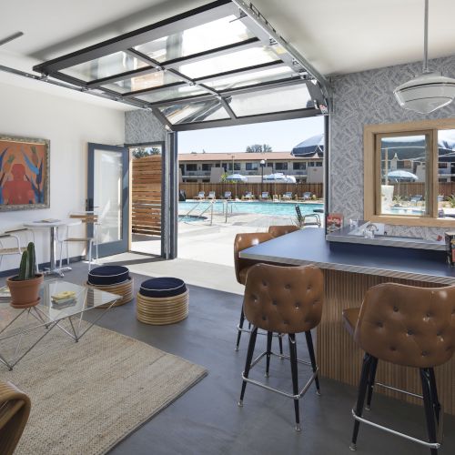 A modern interior space with a glass garage door opening to a pool area, stylish furniture, and a bar counter with stools, ending the sentence.