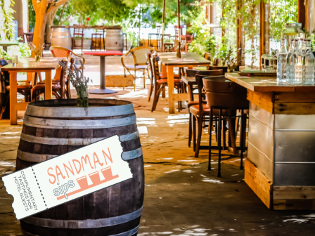 An outdoor seating area of a restaurant with tables, chairs, a wine barrel, and a ticket labeled 